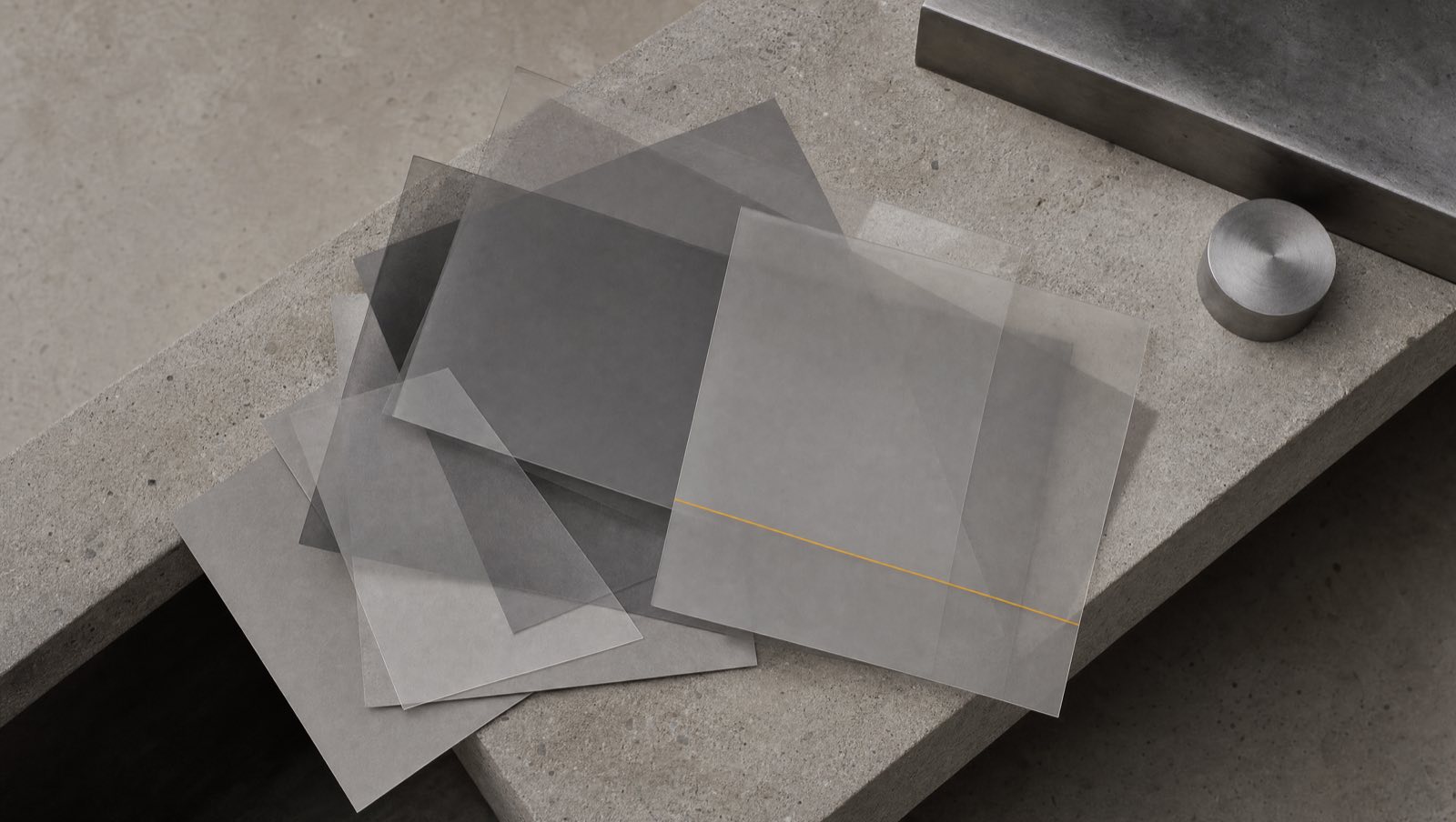 Grey translucent film sheets on concrete, one bearing an amber line