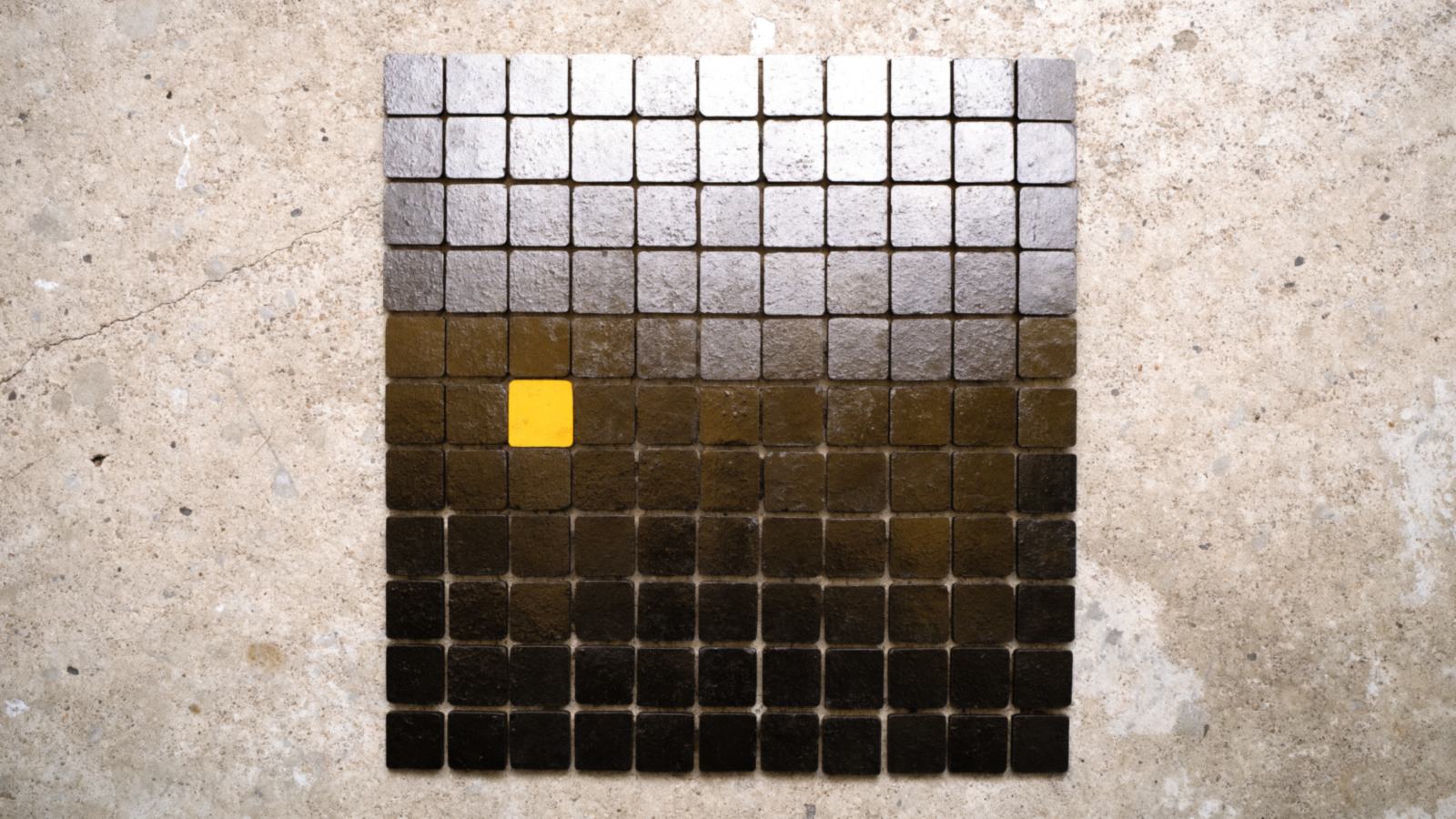 A grid of cast metal patches on concrete, exactly one amber